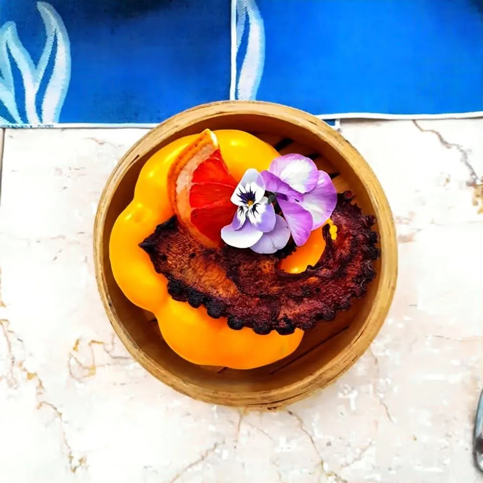 Preparación tostada servida en un cuenco, con piezas amarillas y una flor morada.