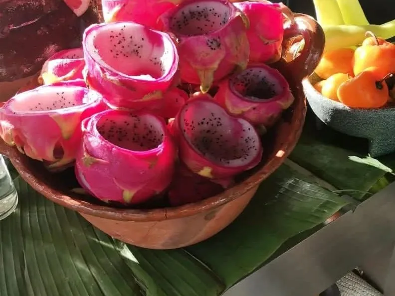 Mitades de pitaya de cáscara rosa colocadas en un cuenco sobre hojas verdes.