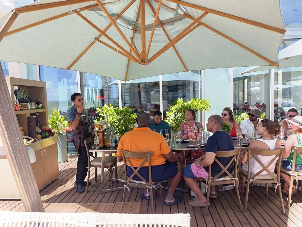 Una persona con mandil explica una degustación a un grupo sentado en una terraza bajo una sombrilla.