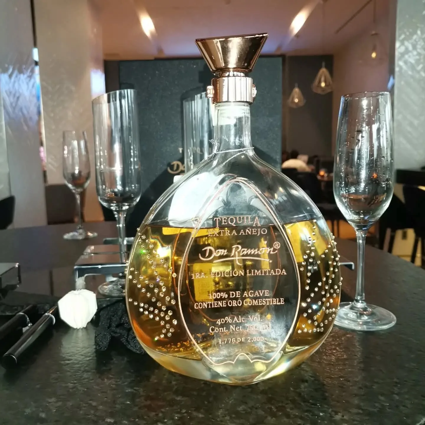 Botella redonda de tequila sobre una barra junto a copas vacías.