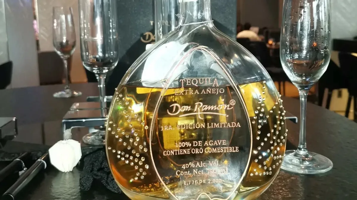 Botella redonda de tequila sobre una barra junto a copas vacías.